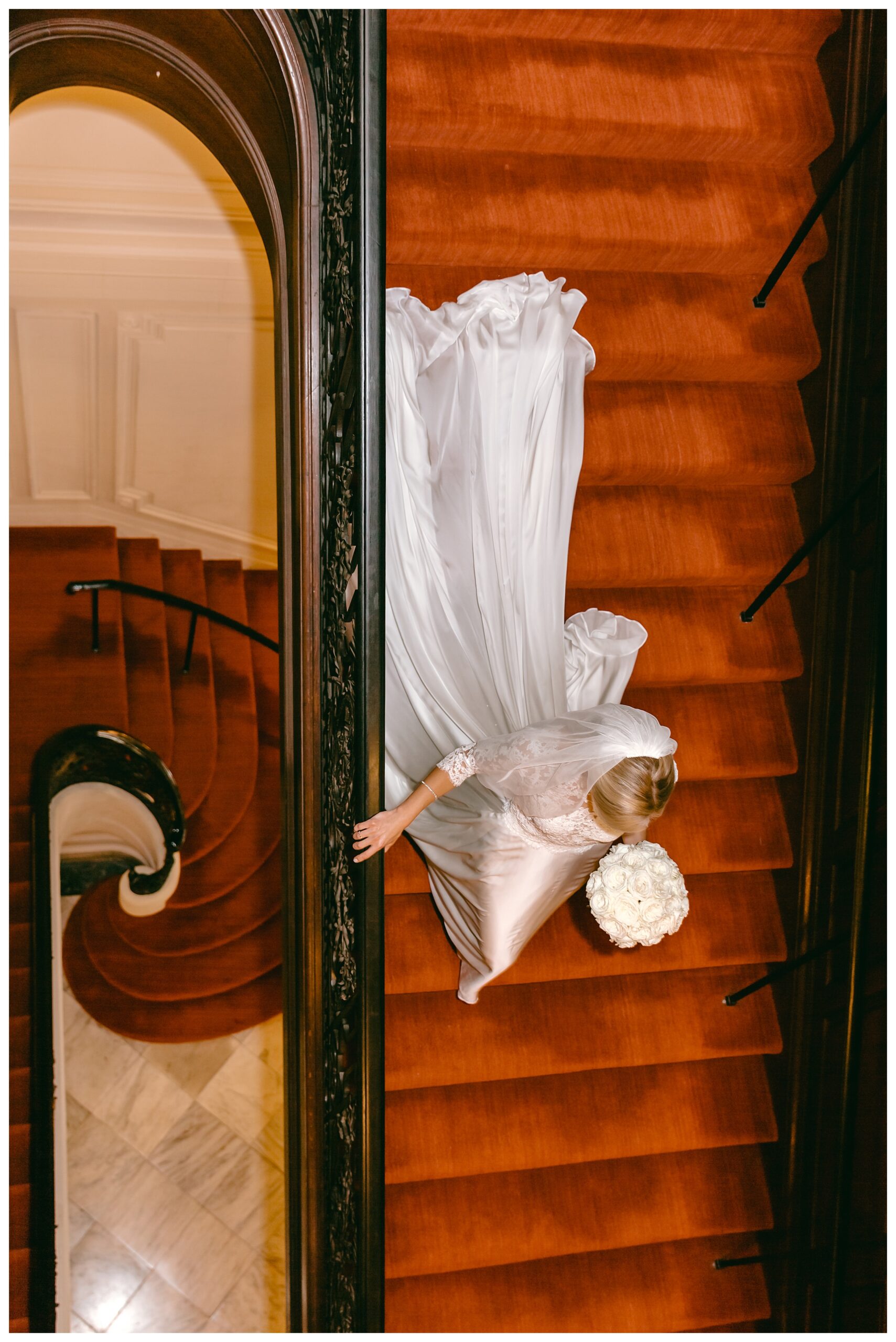 bride from above walking down red carpet of winding stairs