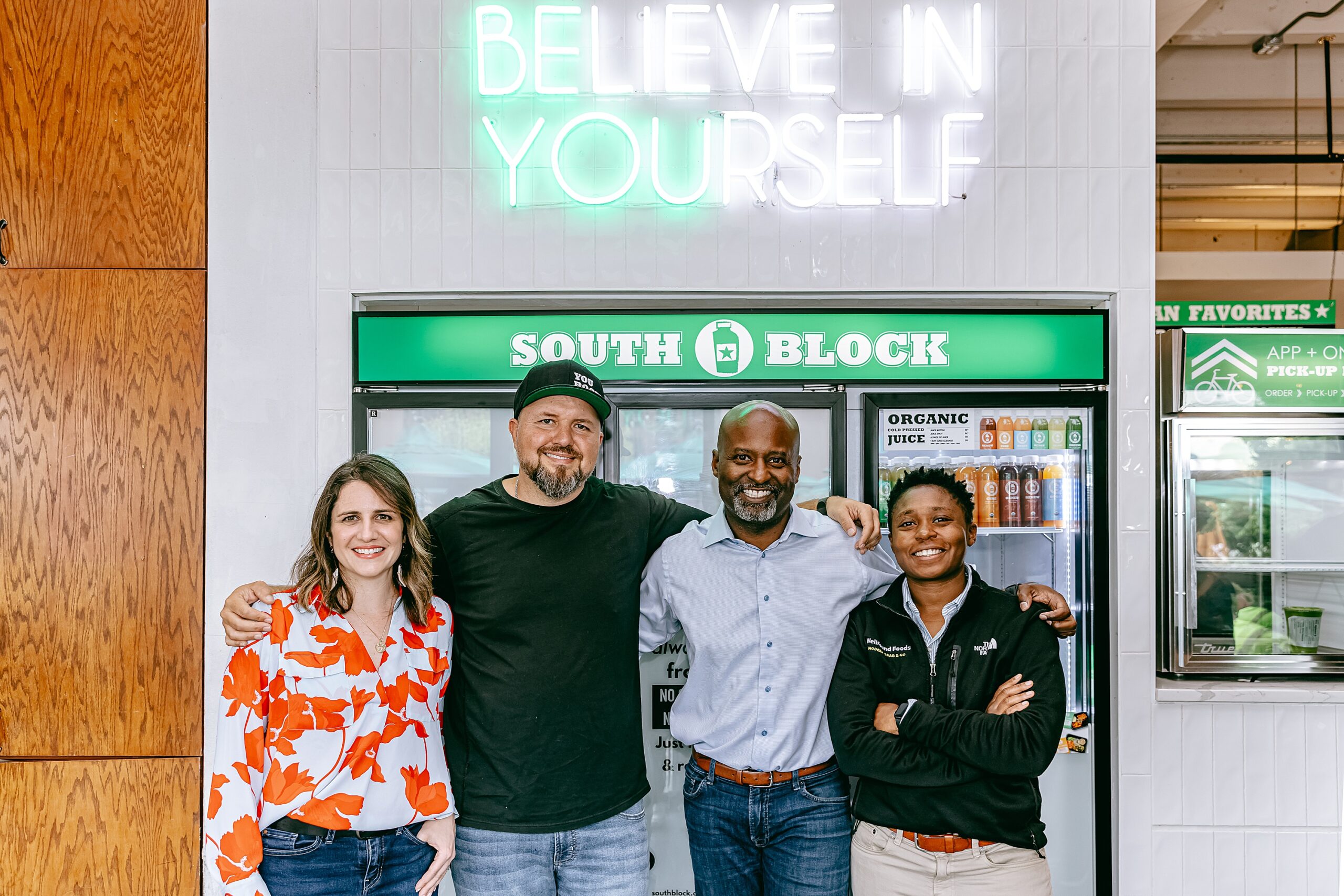 team of four people pose for a photo inside of union market and a fridge for south block smoothie store