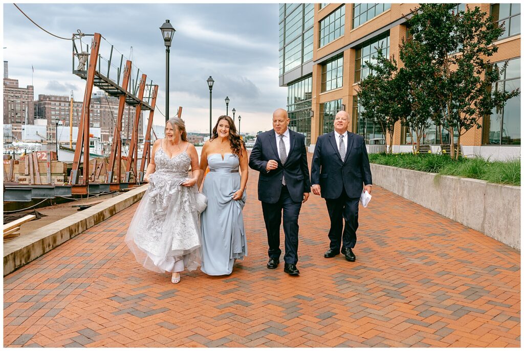 wedding party candid photo of walking towards the camera with pier and harbor in the background with water