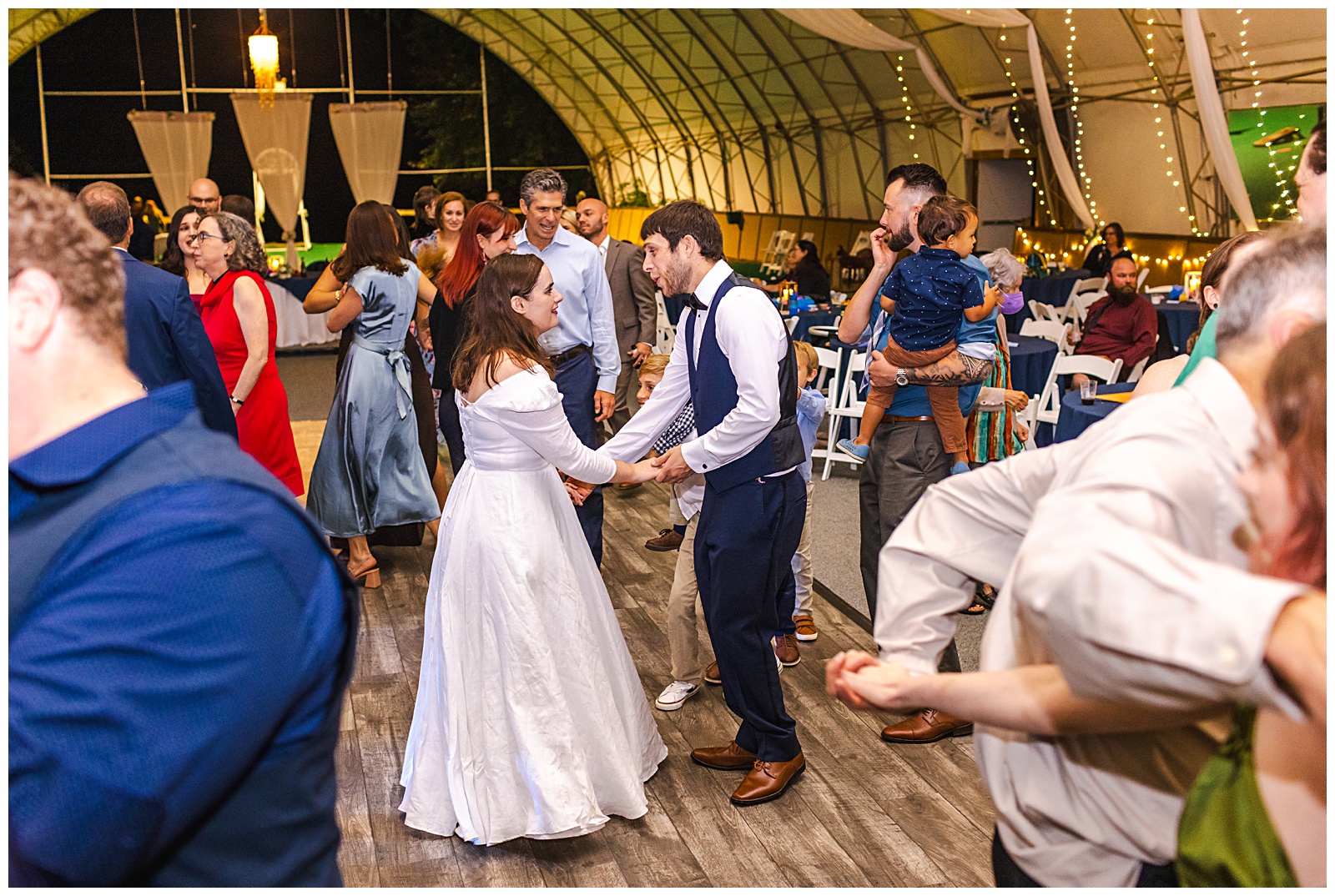 bride and groom dancing in the middle of the dance floor surrounded by their wedding guests all inside a barn reception venue