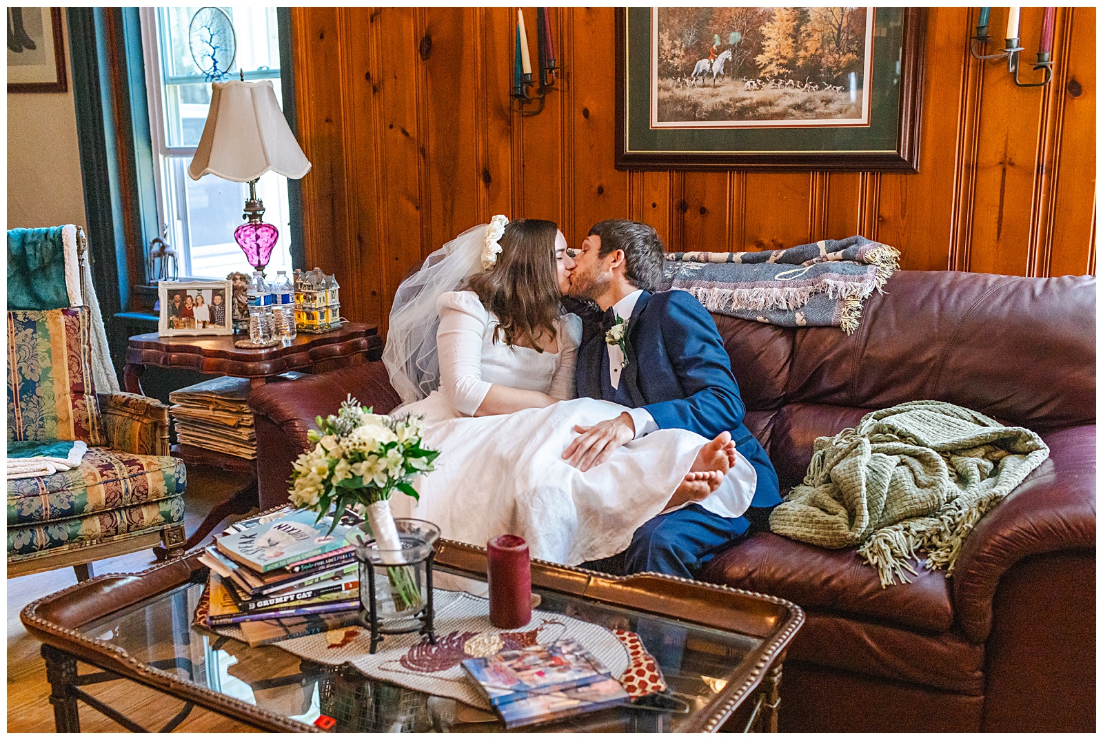 bride and groom kissing on a leather couch on their wedding day