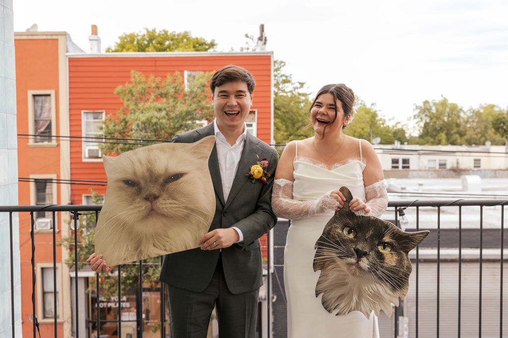 Couple laughing while holding oversized cat cutouts at a playful non traditional wedding in Brooklyn.