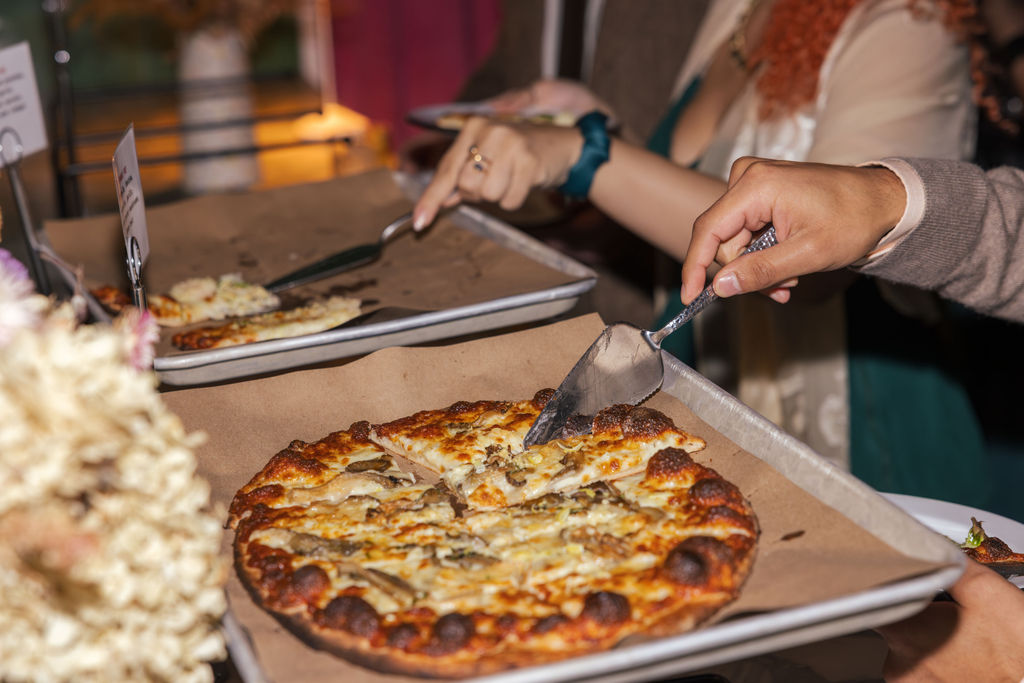 Guests serving pizza during a casual open bar celebration at a non traditional Brooklyn wedding.