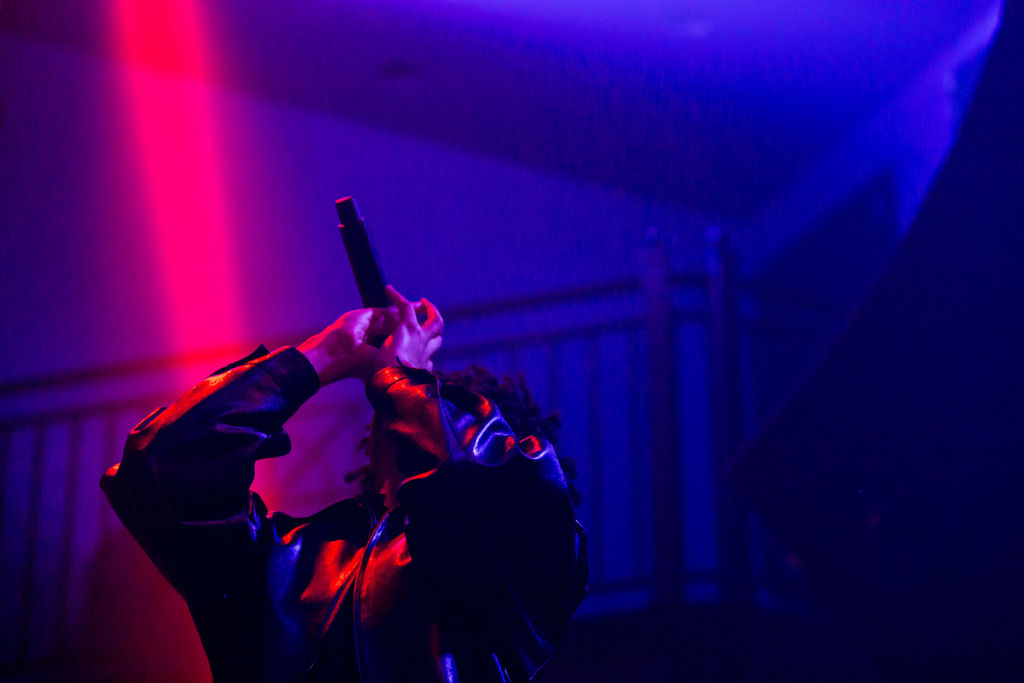 Editorial artist spotlight photograph under saturated red and purple stage lights at the 9:30 Club in Washington DC, evoking a haunting late night mood.