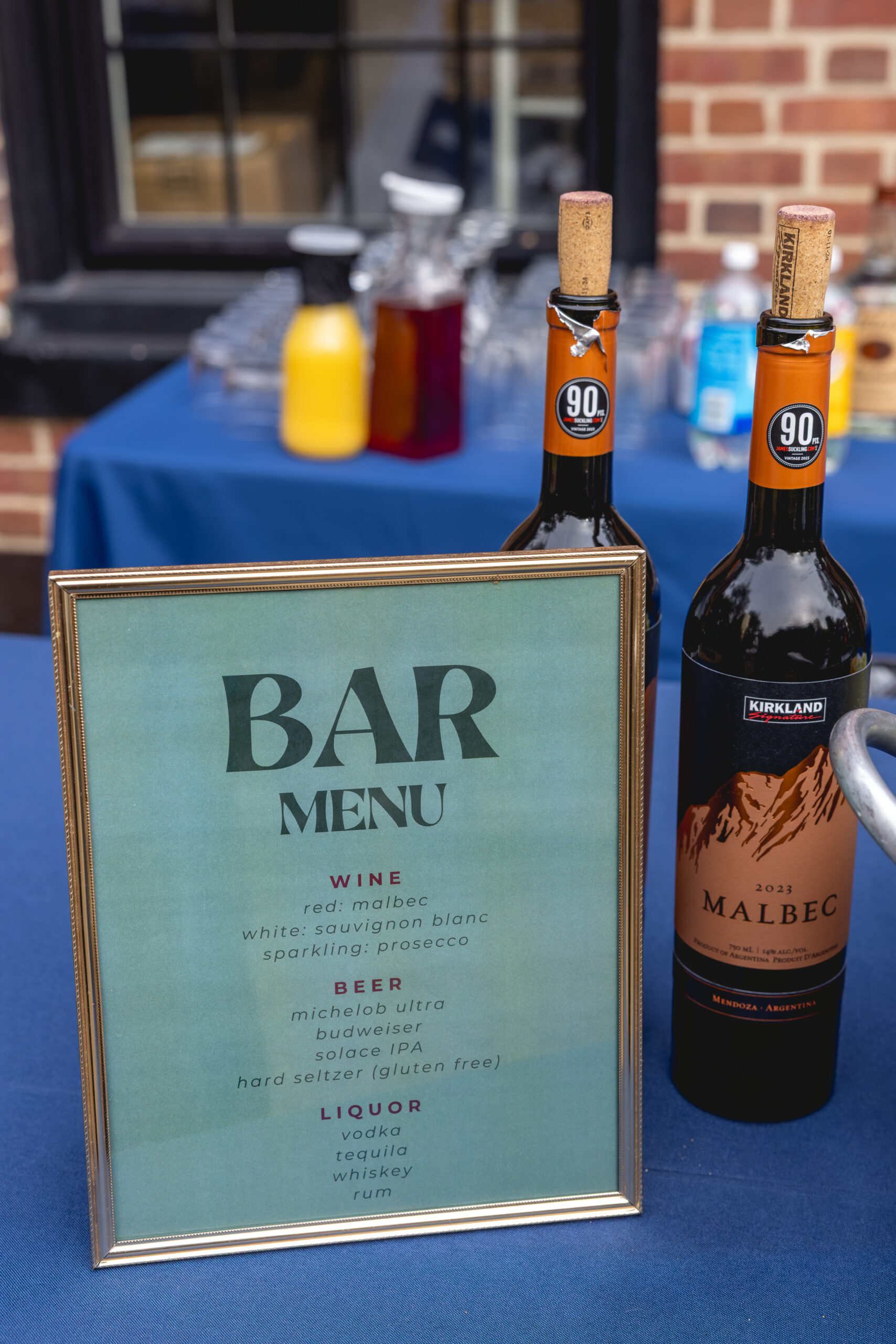 Framed wedding bar menu featuring wine, beer, and liquor options with bottles on blue linen table