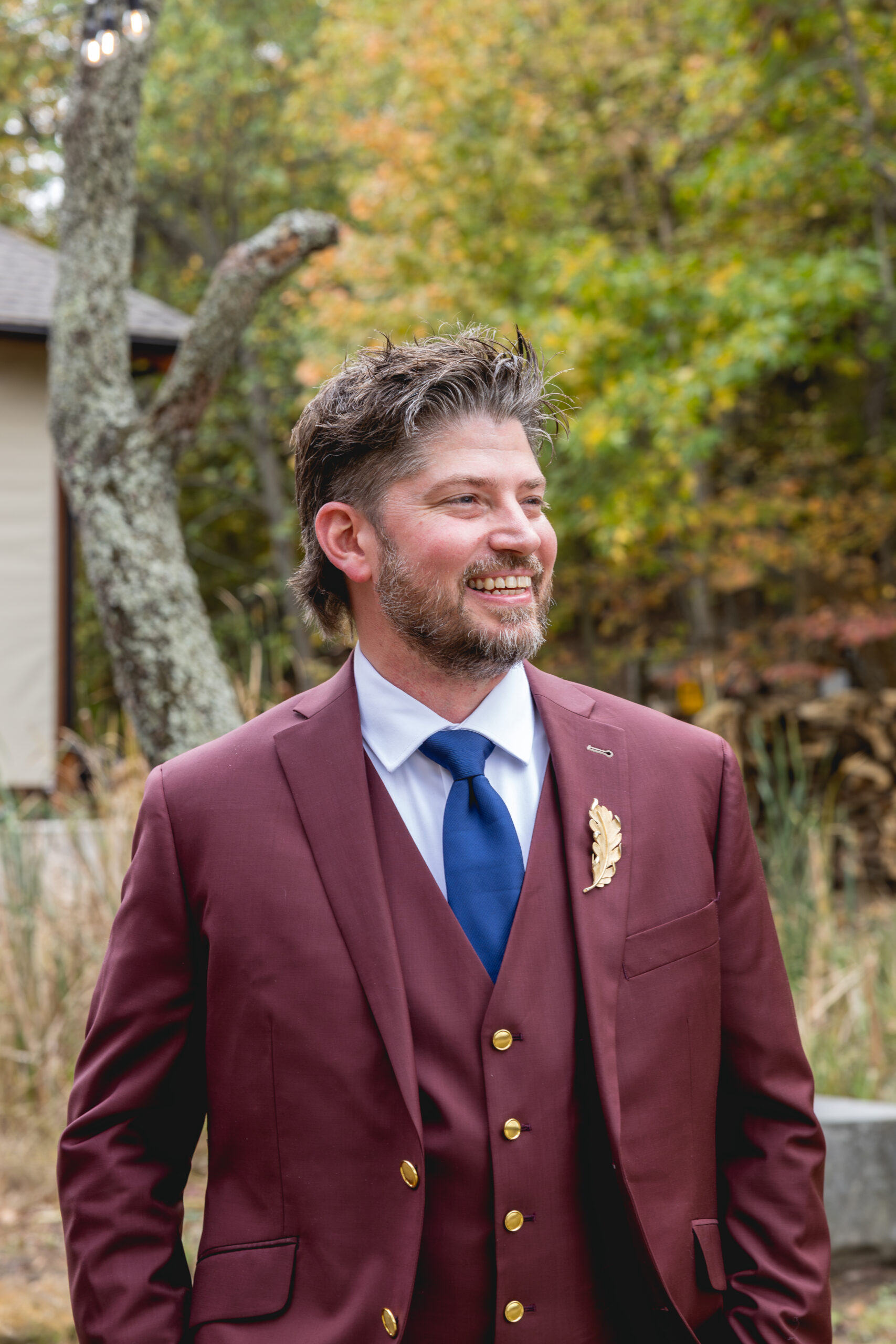 Groom smiling in maroon three piece suit during outdoor fall wedding portraits