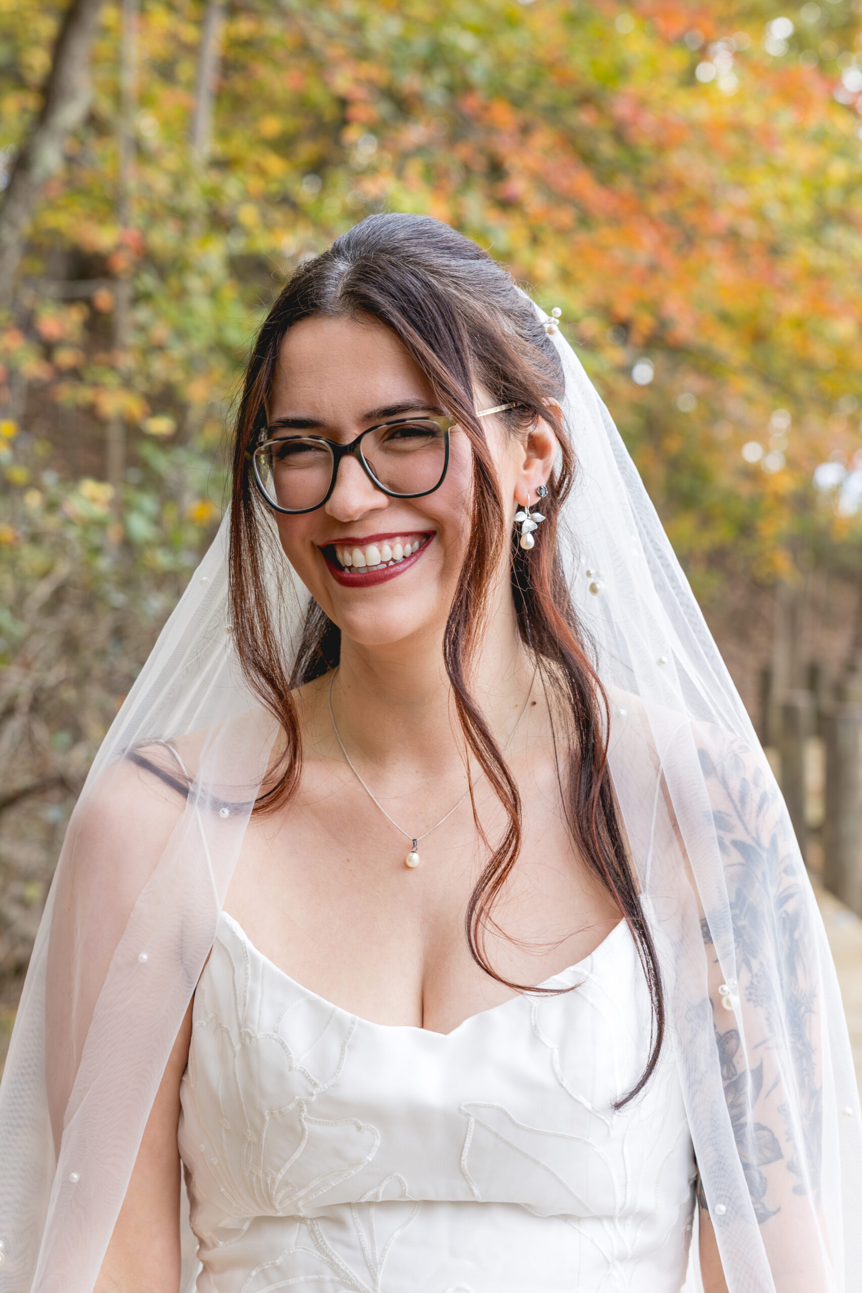 Bride smiling in wedding gown and veil with fall foliage during Annapolis waterfront wedding portraits