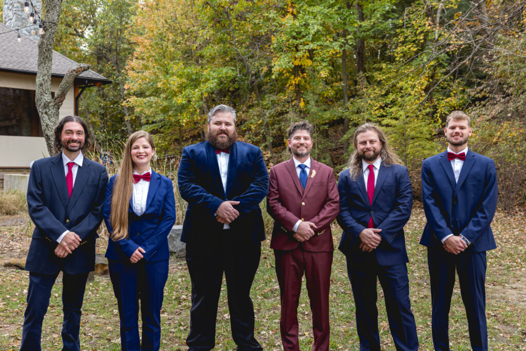 Wedding party portrait with groom in maroon suit and attendants in navy suits with red bow ties