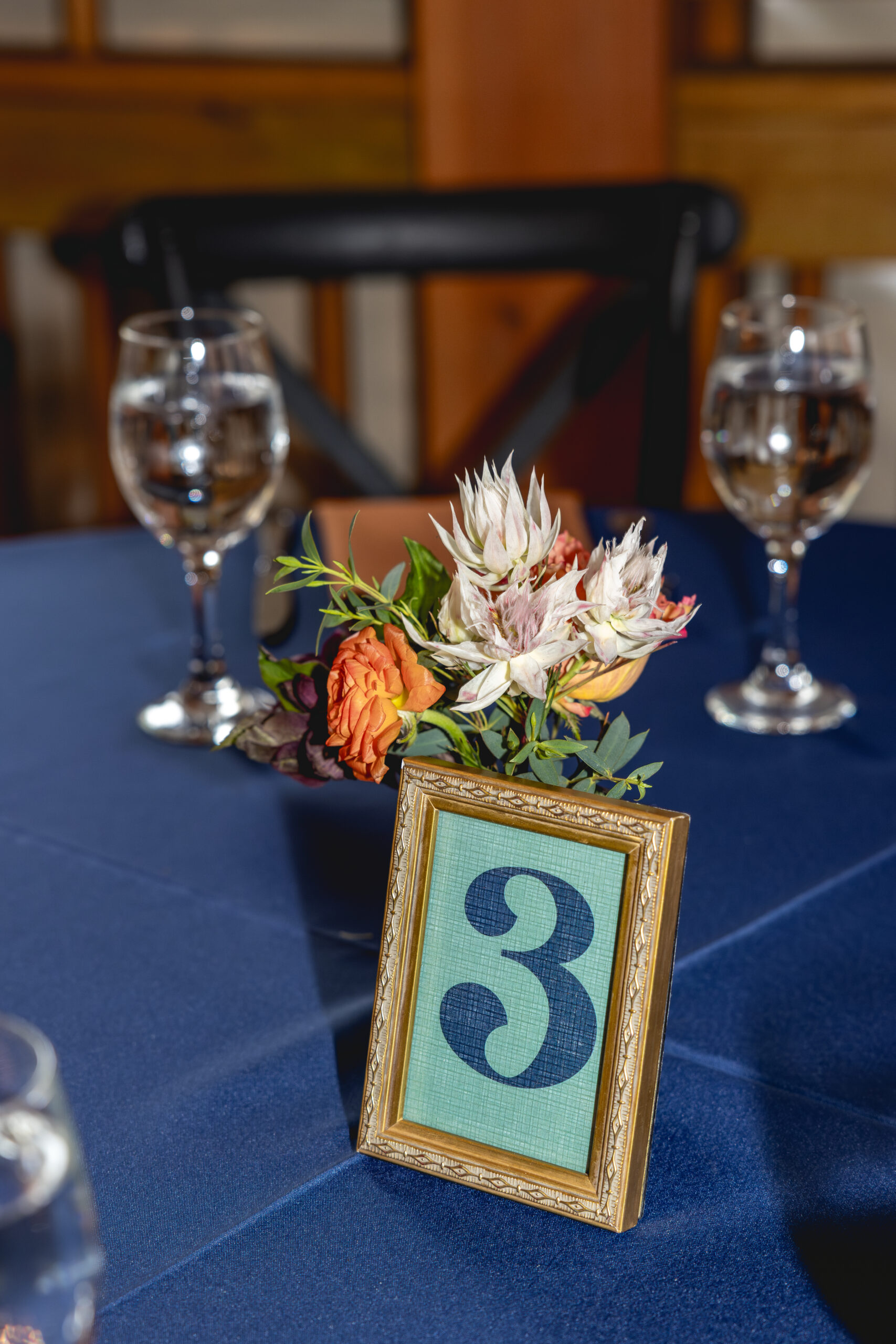 Framed table number with small floral centerpiece and navy linens at reception