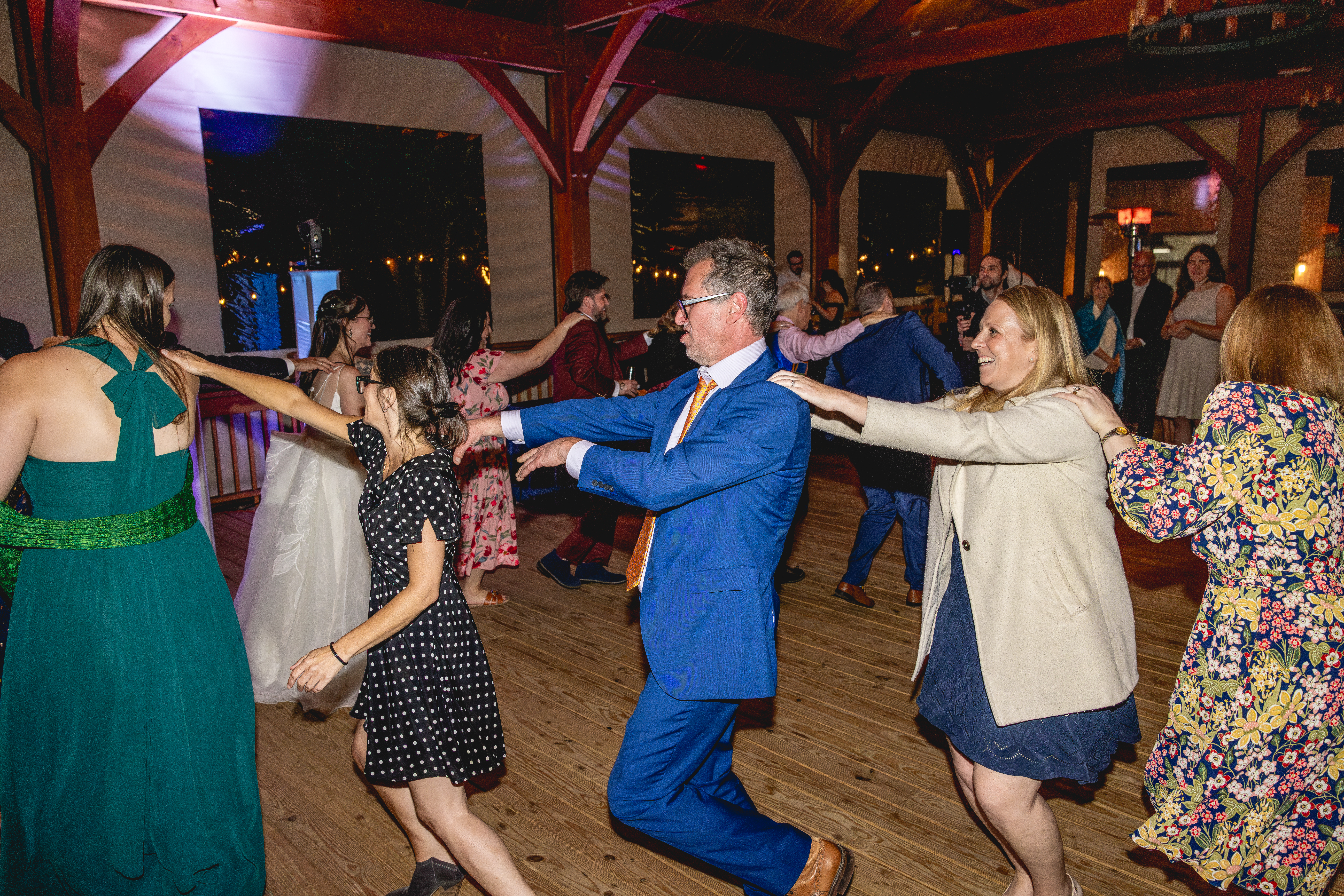 Guests laughing and dancing in a conga line inside the wooden pavilion during the wedding reception