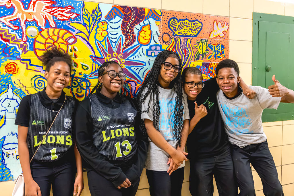 Happy after-school students posing together in front of colorful mural through documentary school photography at Excel Upper School