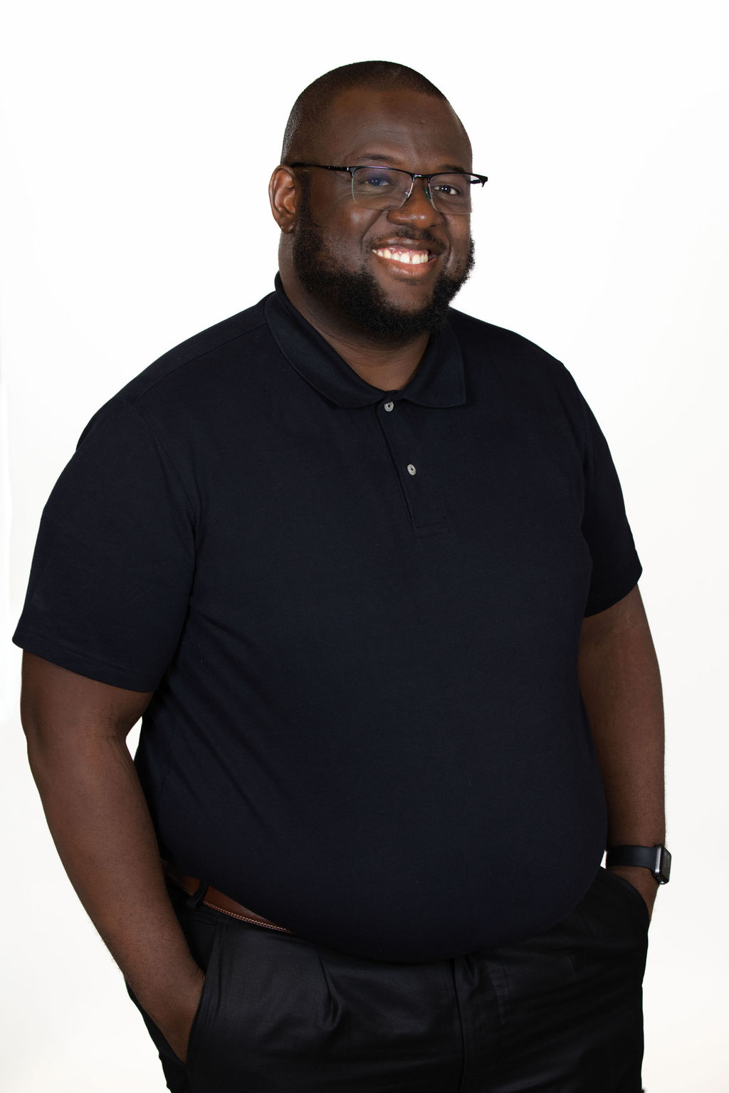 Professional headshot of a bald man wearing glasses and a navy polo shirt, smiling on a white background by Liz Stewart Photography DC