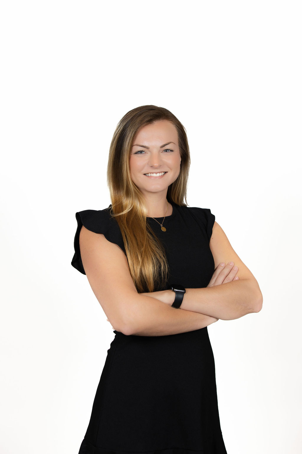 Corporate headshot of a young woman with long straight blonde hair wearing a black ruffled dress, arms crossed, white background by Liz Stewart Photography DC