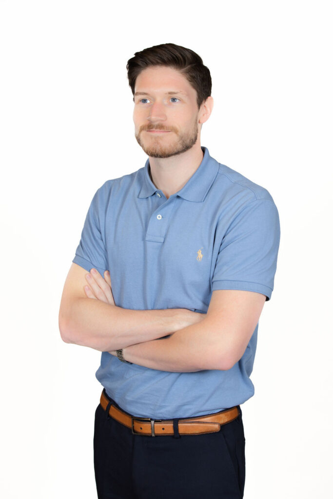 Full body professional headshot of a man with dark hair and a beard wearing a blue polo shirt, arms crossed, white background by Liz Stewart Photography DC