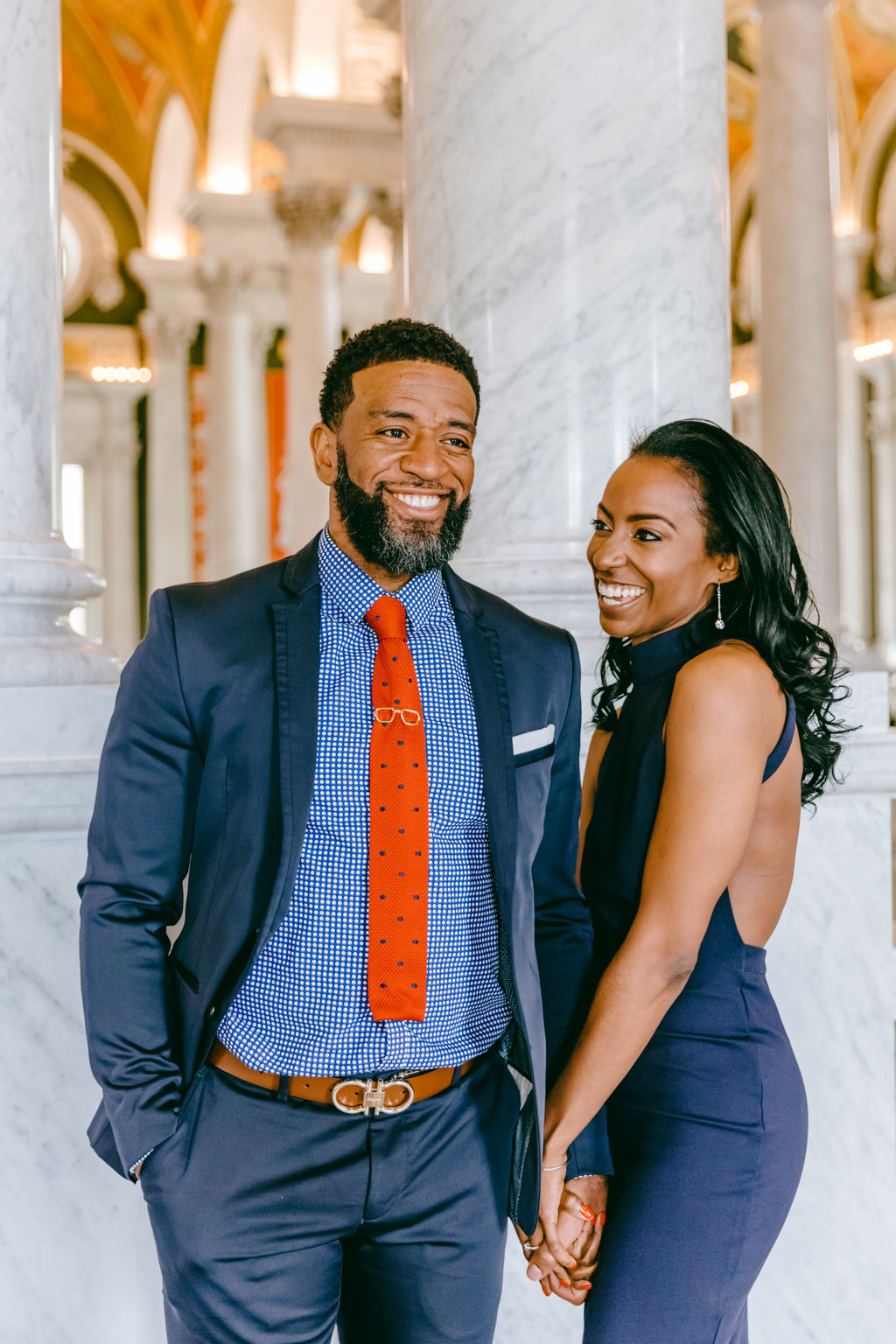 Candid portrait of a couple laughing together in the Great Hall of the Library of Congress, with golden painted arches and marble columns stretching behind them