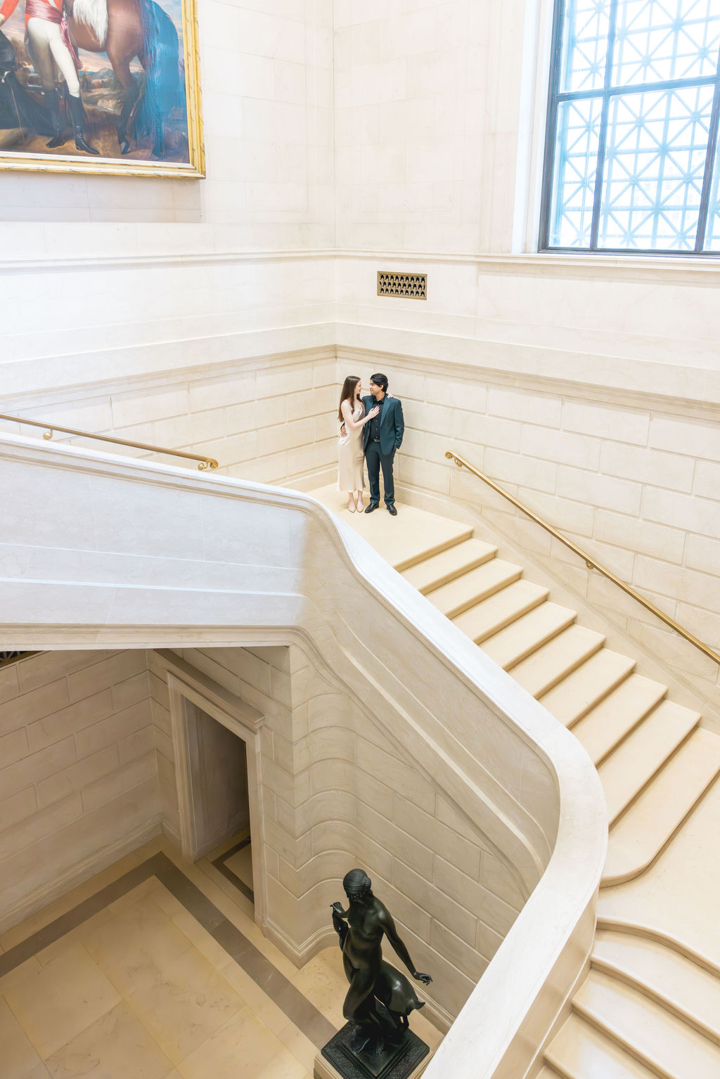 Aerial view of an engaged couple pausing on the curved marble staircase at the National Gallery of Art, a top indoor photoshoot location in Washington DC