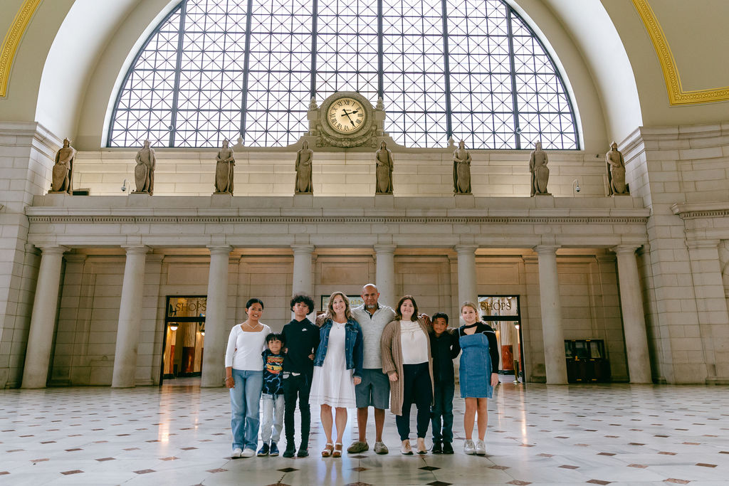 Extended family group portrait inside the main hall of Union Station in Washington DC, with gold-trimmed arched ceilings and classical statues visible overhead