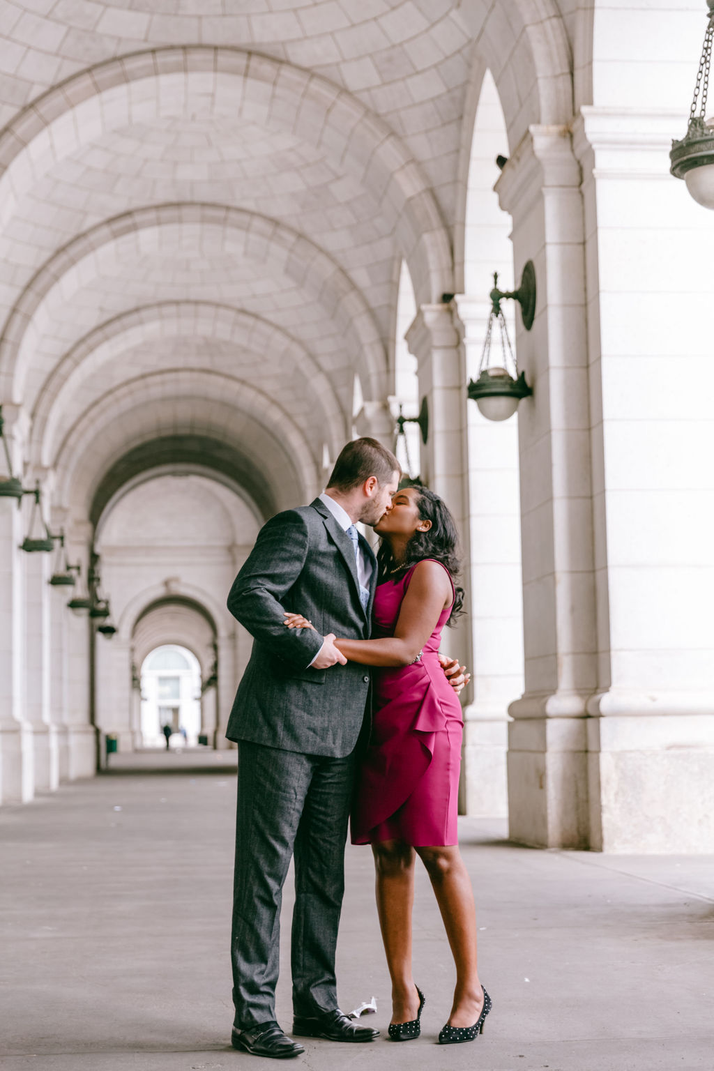 Engaged couple sharing a kiss under the stone arched colonnade at Union Station in Washington DC, a prime photoshoot location.