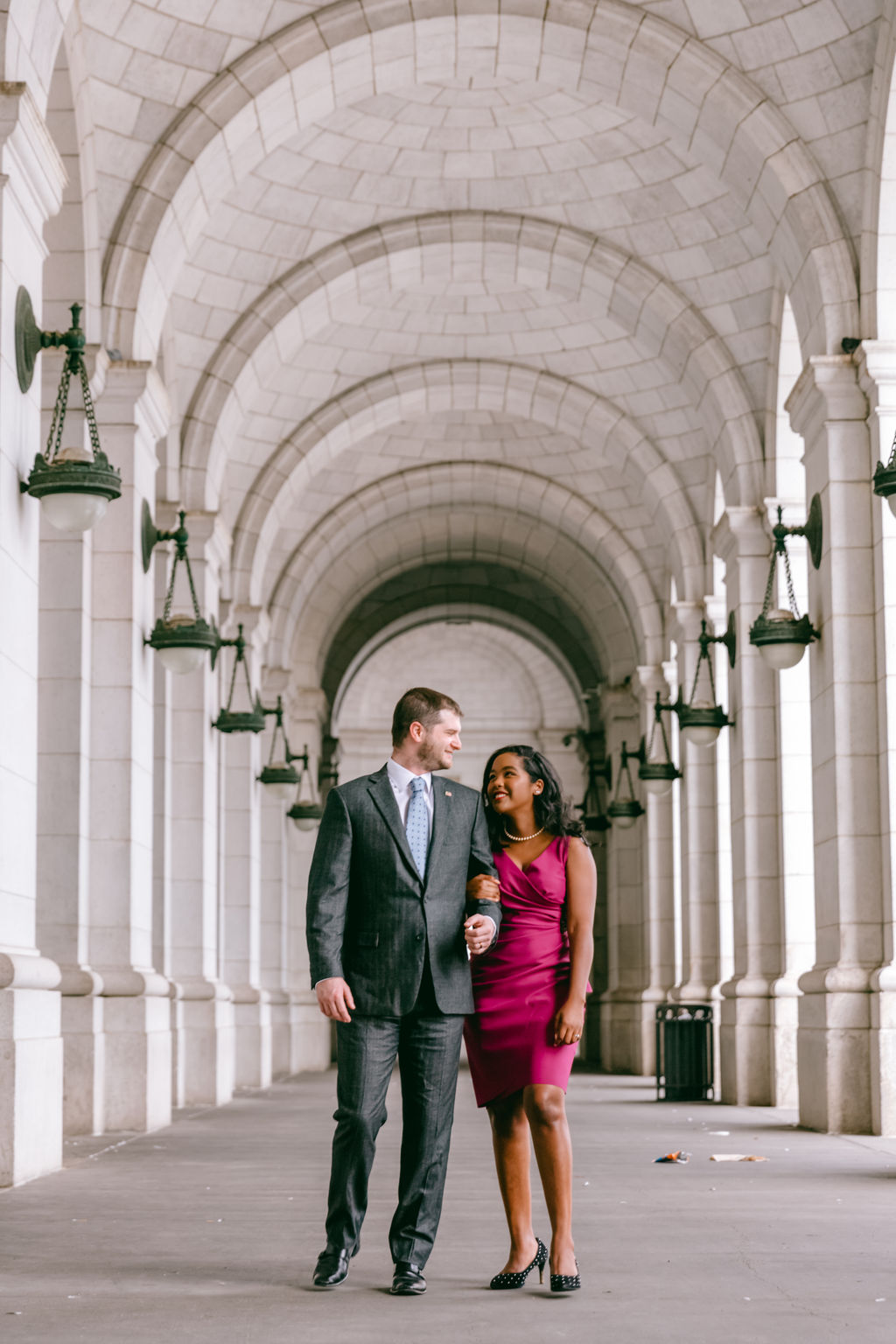 Couple embracing and smiling in the main hall of Union Station in Washington DC, framed by the iconic arched window and historic clock above them